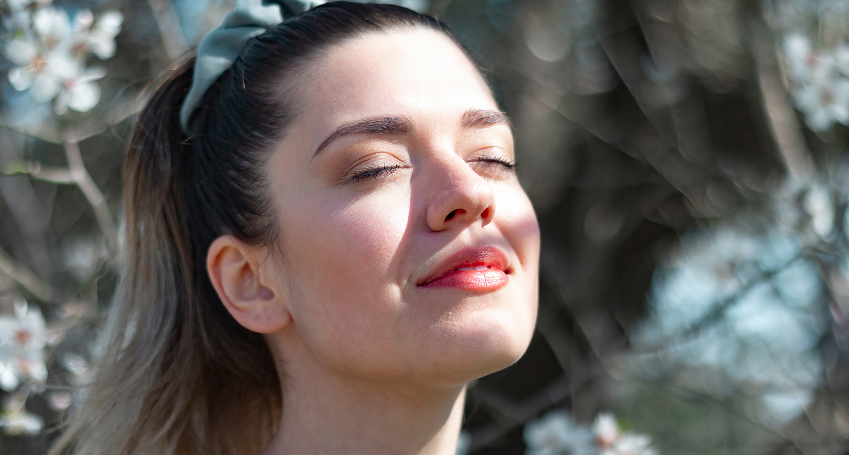 Smiling woman with eyes closed enjoying the sun among blossoming trees