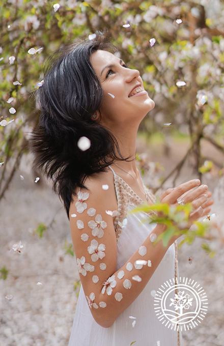 Smiling woman looking up at blossom petals falling in an orchard