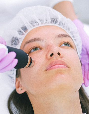 Woman in a hair cap receiving a device treatment below her eye