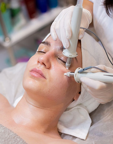 Woman lying back as a provider treats her face with two handheld devices