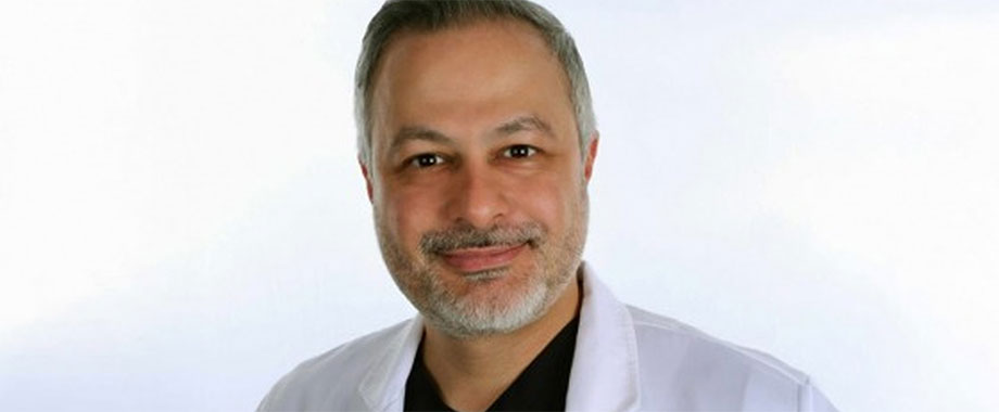 Dr. Amin Esfahani in a white coat over black scrubs