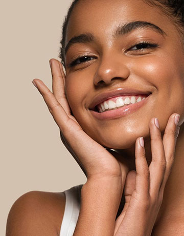 Smiling woman with even, glowing skin framing her face with her hands