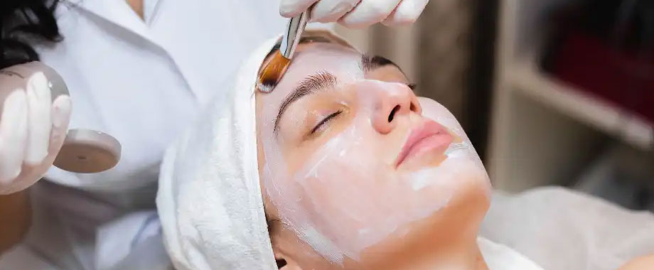 Provider brushing a white mask onto a woman's face during a facial treatment