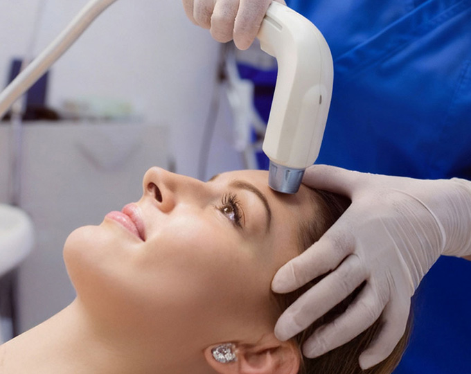 Gloved provider treating a woman's forehead with a handheld device