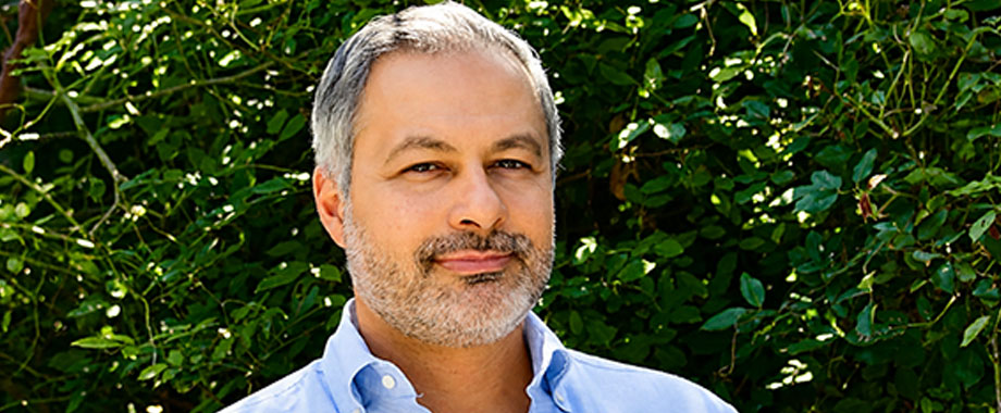 Smiling man with a grey beard in a blue shirt, outdoors